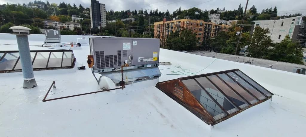 Completed white TPO membrane roof at Grand Prix Motor Cars in Portland, OR, with HVAC curb flashing, a vent stack, and a vintage gabled skylight against the urban hillside