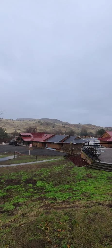Wide view of Kah-Nee-Ta Resort and Spa in Madras, OR, with bright red standing seam metal roofs across multiple lodge gables, a darker charcoal standing-seam section, and arid Central Oregon hills under overcast sky