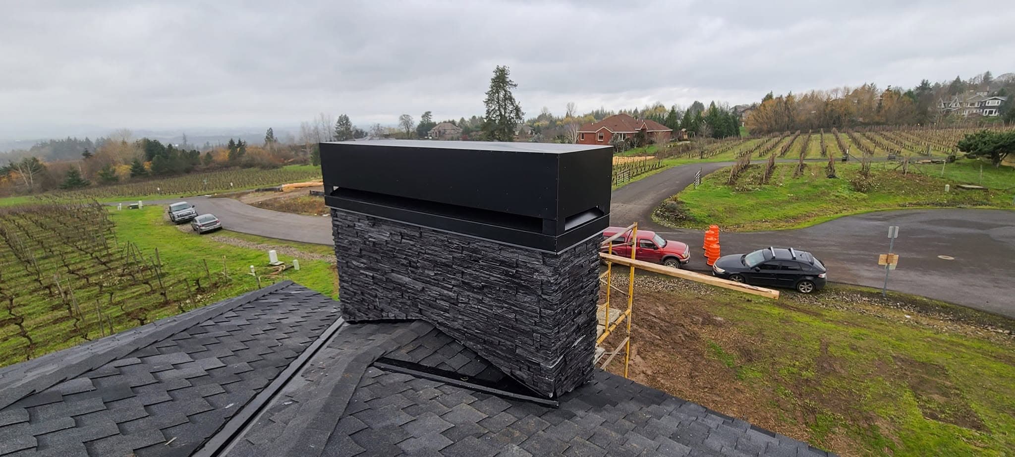 Chimney with stone cladding and metal cap on an asphalt shingle roof