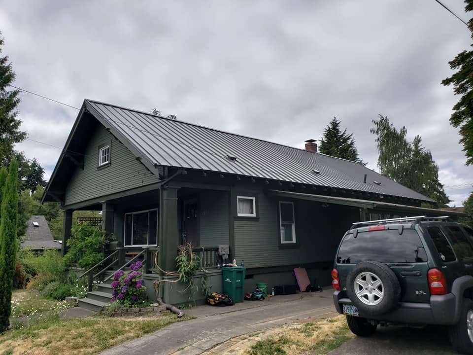 Tan standing seam metal roof on a two-story home among evergreens