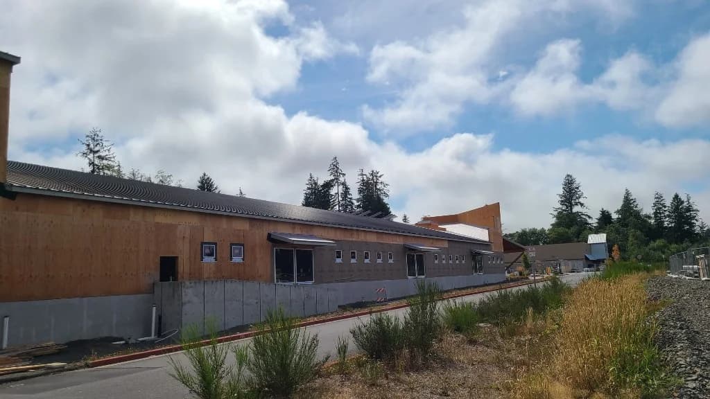 Side elevation of Roby's Furniture Store in Warrenton, OR, mid-construction, with dark standing seam roofing over house wrap and siding in progress
