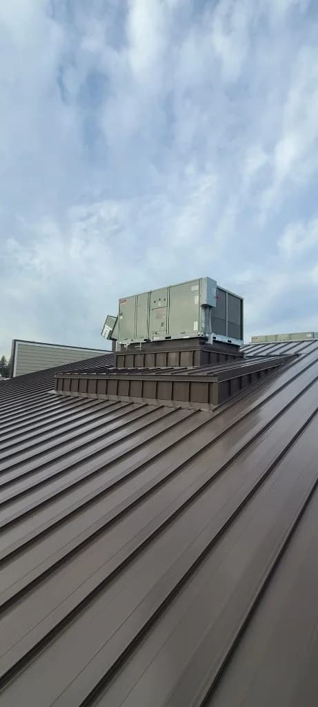 Close-up of bronze standing seam panels and a rooftop HVAC unit on a custom flashed metal curb at Roby's Furniture Store in Warrenton, OR