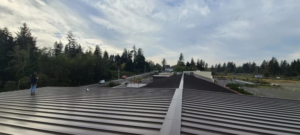 Bronze standing seam metal roof at Roby's Furniture Store in Warrenton, OR, viewed from the ridge with a worker for scale and the commercial corridor beyond