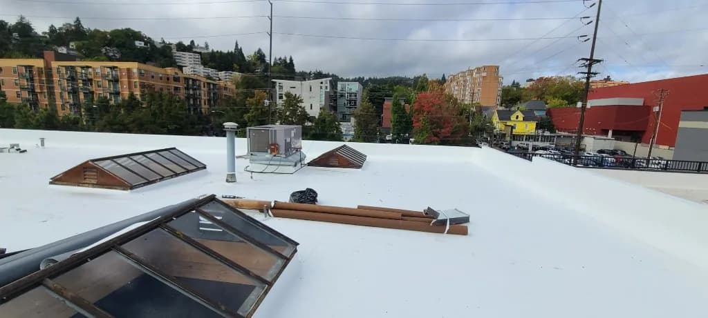 Wide TPO roof field at Grand Prix Motor Cars in Portland with three peaked skylights, an HVAC unit, and rolled material on the completed membrane