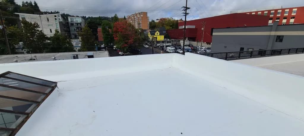 Parapet wrap and skylight flashing on the Grand Prix Motor Cars TPO roof, with a Portland parking lot and hillside buildings beyond