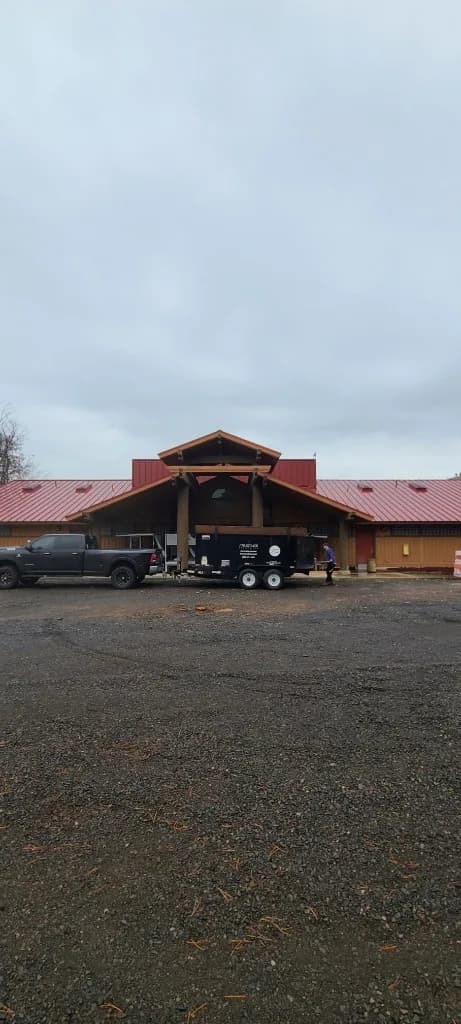 Lodge entrance at Kah-Nee-Ta Resort and Spa in Madras, OR, with a bright red standing seam roof, timber columns, circular gable window, pickup, and a field trailer on the gravel lot